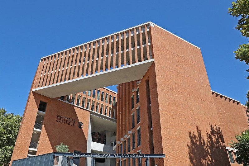 Façade en brique de la Toulouse School of Economics, vue en contre-plongée sous un ciel bleu